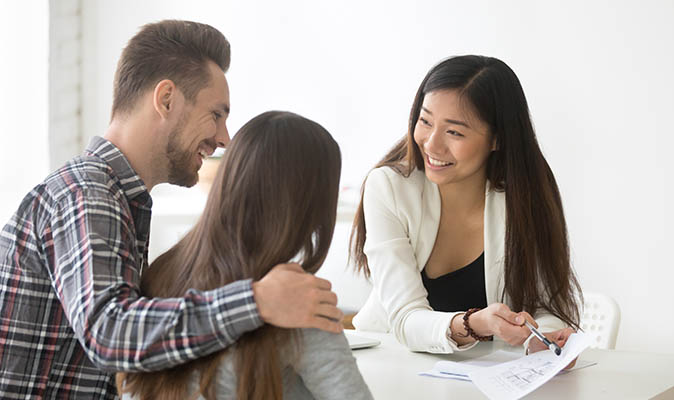Potential homebuyers sit at a desk and look over paperwork with a real estate agent.