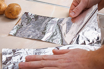 A person’s hand preparing food using aluminum foil sheets 