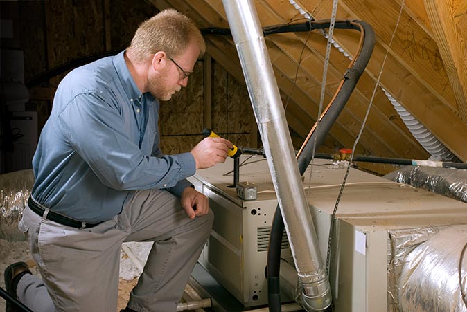 A technician inspects a furnace in the ceiling of a home with a flashlight