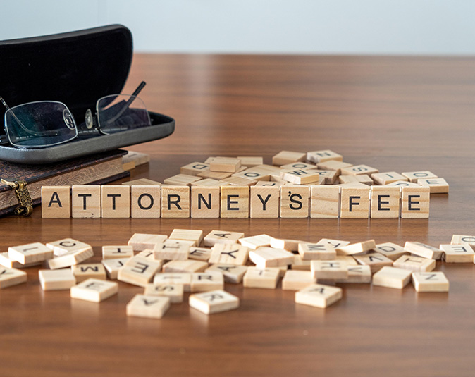 Attorney’s fee word represented by wooden letter tiles on a wooden table with glasses and a book.