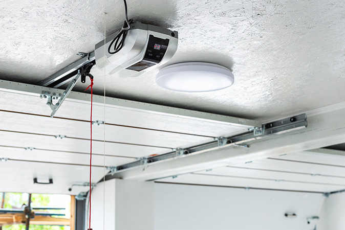 Image shows a garage interior with a partially opened door and a new automatic garage door opener mounted to ceiling.