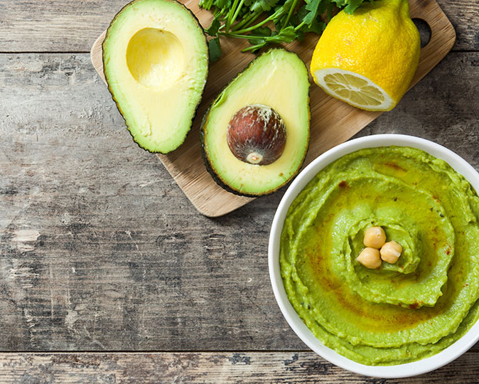 Festive bowl of green avocado hummus served with a lemon.