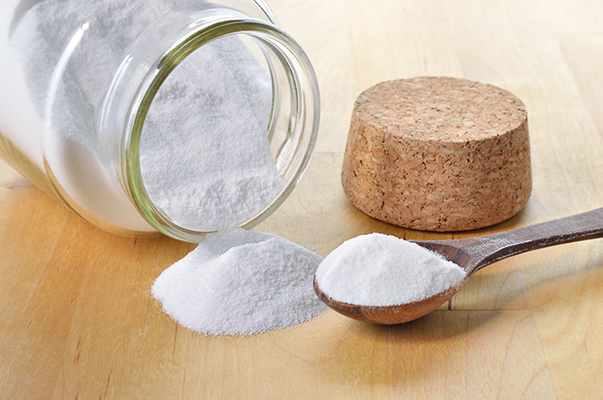 Image shows bottle of baking soda on its side with spoonful of the powder on spoon.