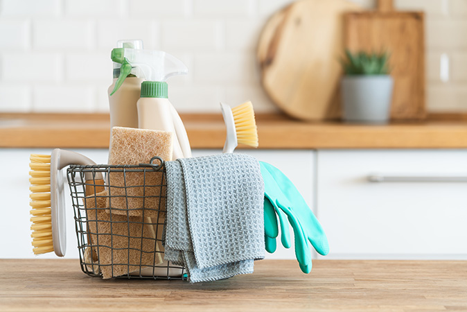 A basket with brushes, microfiber cloth, natural sponges, and cleaning products in a kitchen.