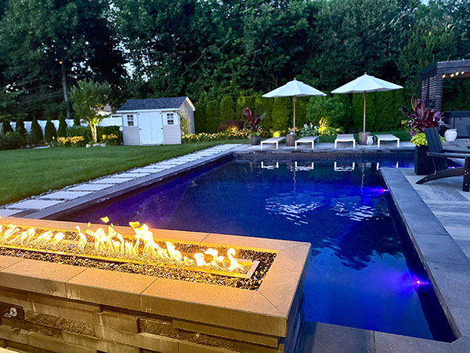Beautiful outdoor fire table sitting near the edge of a swimming pool as the sun goes down.