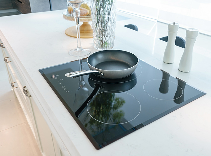 A cooking pan sits on a black induction cooktop set on a white counter.