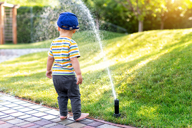 A child watches a properly working lawn sprinkler watering a front yard.