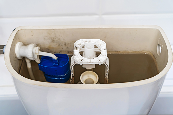 A close-up image of a broken toilet tank and the cover off..