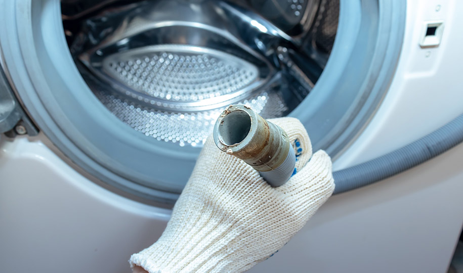 A plumber holding a broken flexible drain hose of a washing machine.