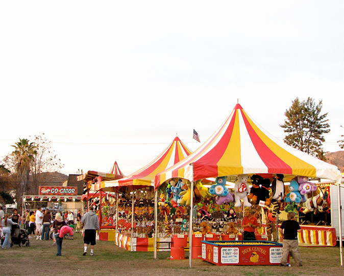 A small carnival with game booths, rides, and people wandering around.