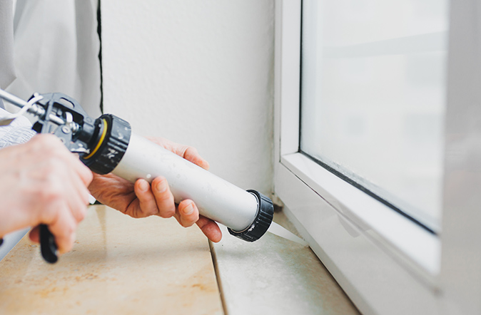A worker using a caulking gun to caulk a window frame.