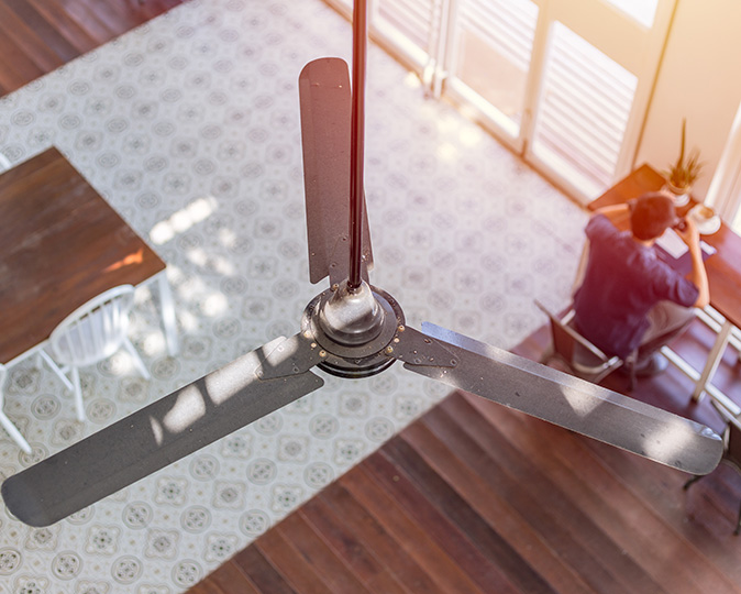 A man works at his desk under a ceiling fan. 
