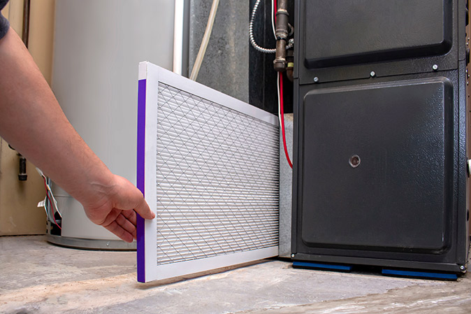 A homeowner changing the air filter on a furnace in a basement.