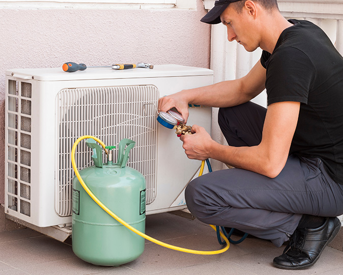 An HVAC service technician checks AC refrigerant levels in condenser unit.