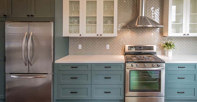 Gray chevron patterned backsplash with teal cabinets below it.