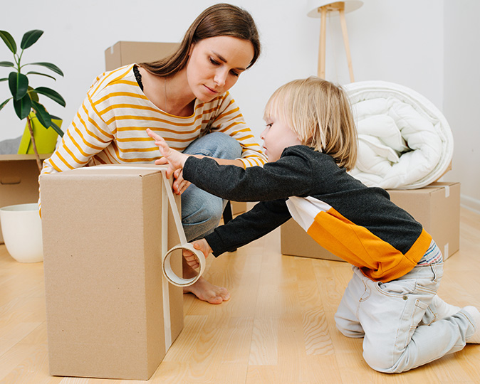 A boy helps his mother pack by taping up a box.