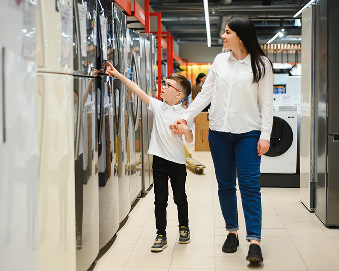 A mother and child peruse the refrigerator section of an appliance store.