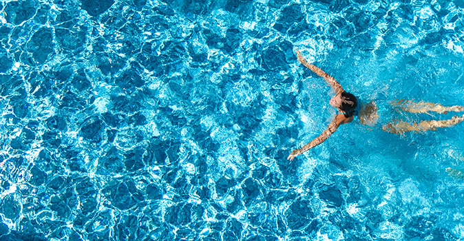 An aerial view of a woman swimming in a home swimming pool after the pool has been cleaned.