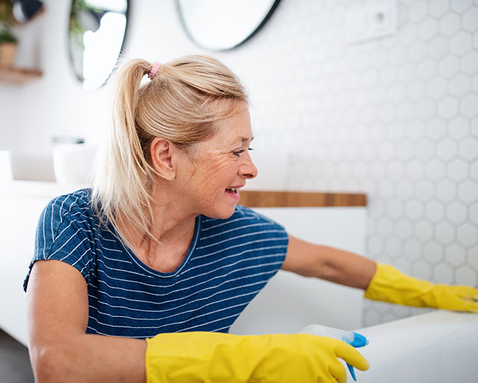 Homeowner cleans bathtub in modern white bathroom.