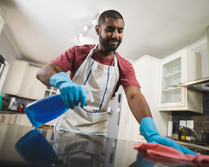 A man wearing gloves cleans the marble counter in his kitchen.