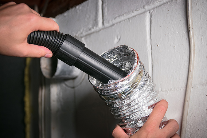A close-up of a person’s hand vacuuming an aluminum dryer vent hose.
