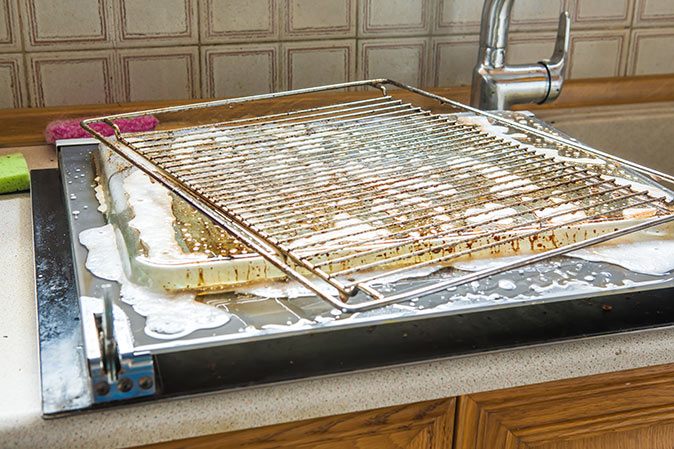 A dirty dish rack being washed in a soapy kitchen sink.