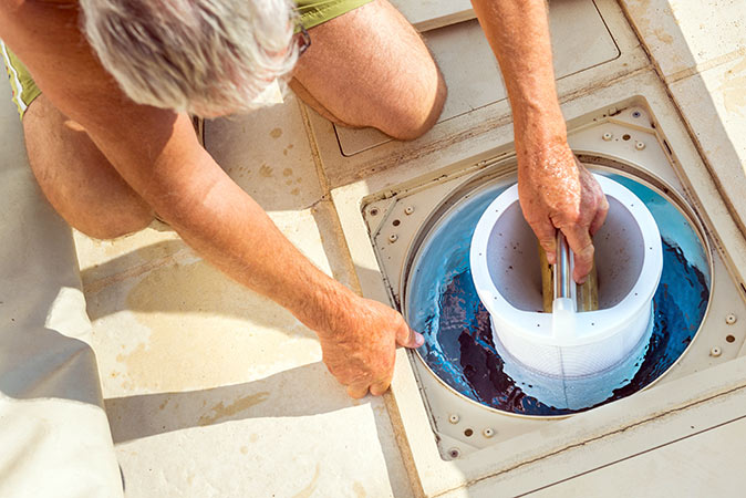 A person kneeling down and removing a pool filter. 
