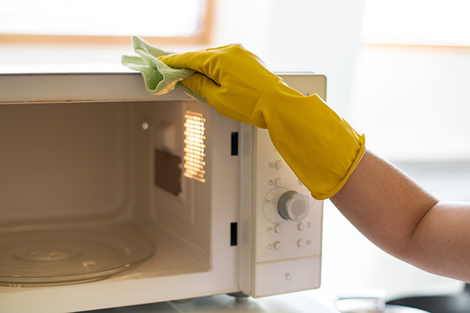 Person wearing yellow gloves is cleaning the top of a microwave.