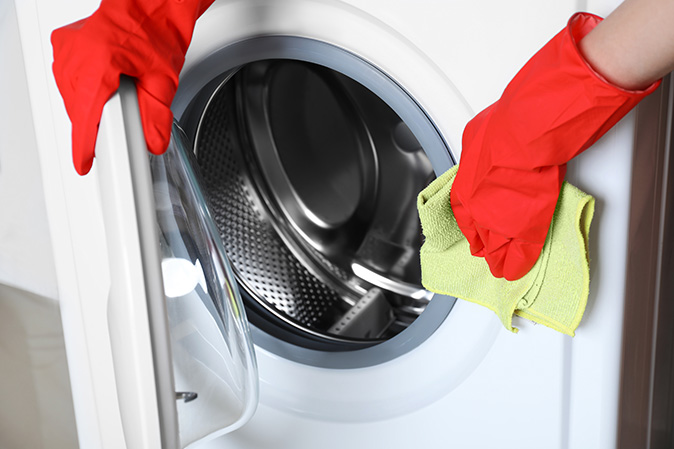 A woman cleaning a washing machine with rag to prevent mold build-up.