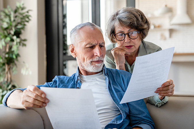 An older couple sits in their home comparing pieces of paperwork.