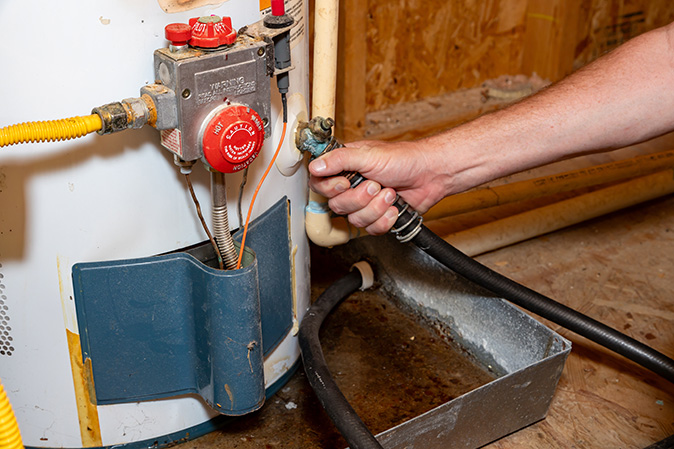 A person’s hand touching a water supply line while water drains from a water heater.