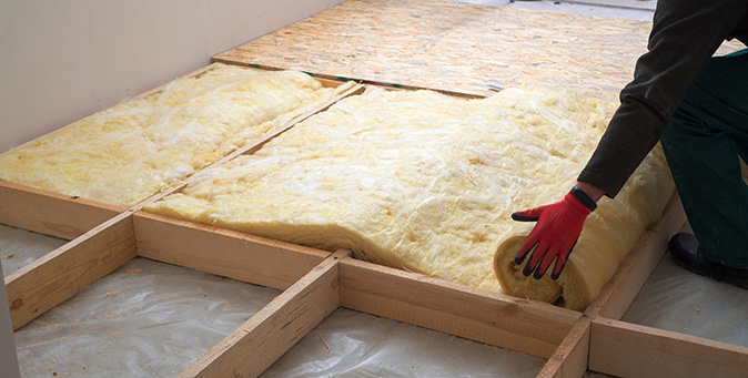 A man wearing red gloves rolling out insulation on the attic floor.