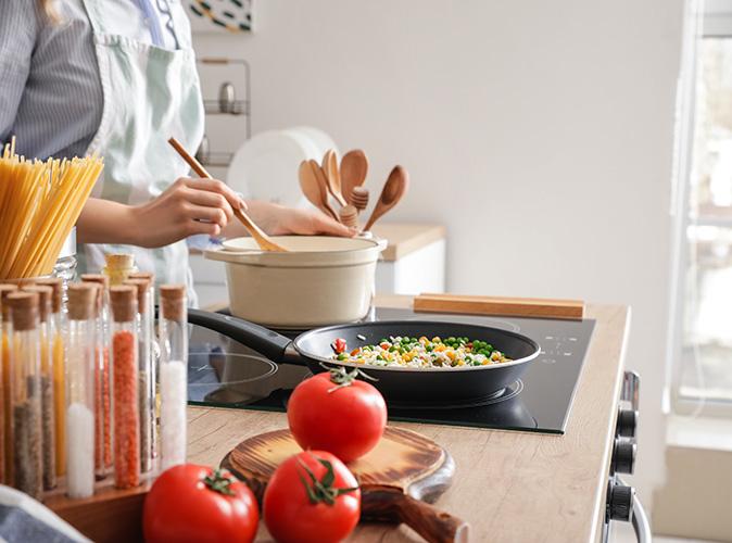 A woman in an apron cooks stir-fried rice on an electric range top surrounded by fresh ingredients. 
