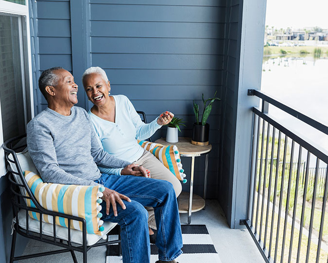 A happy retired couple sits and laughs on the balcony of their condo.