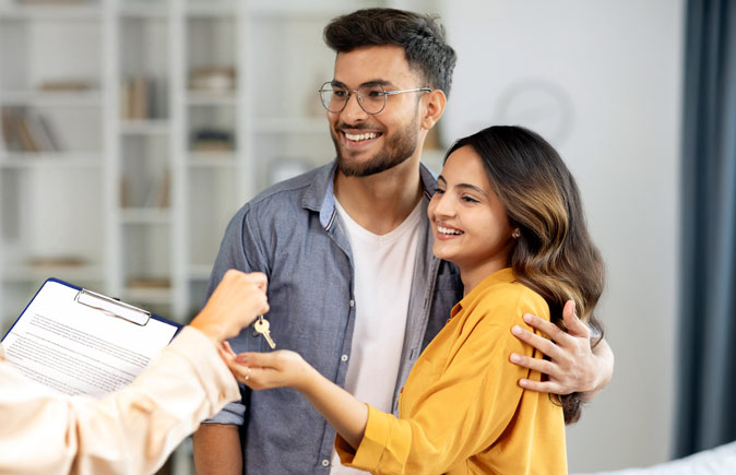 Happy homebuyers smile as they receive key to their new house from their agent.