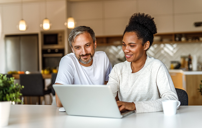 A couple sitting at a table looking at a laptop.
