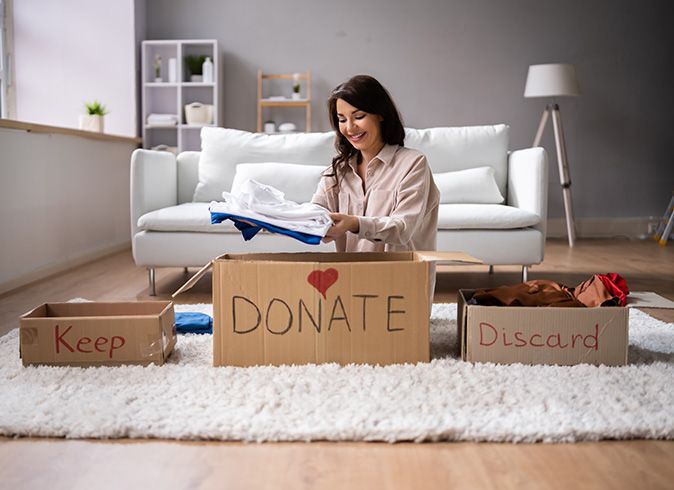 A woman declutters her closet and organizes her clothing in her living room.