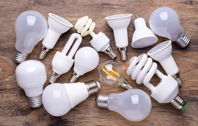 Different types of light bulbs spread out on a wooden table.