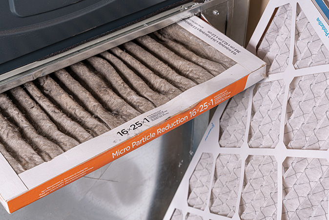 A dirty filter sticks halfway out of an HVAC unit while a clean replacement filter sits propped up next to it.