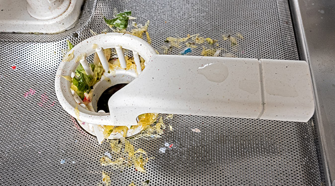 Image shows stainless steel dishwasher tub with food debris in the filter.