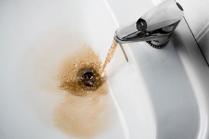 Dirty, brown water running out of a bathroom sink faucet.