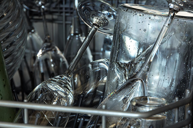 A closeup of wet champagne flutes and drinking glasses in a dishwasher.