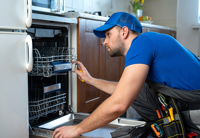 A repairman fixes a dishwasher in a kitchen.