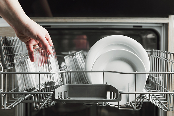 A person’s hand taking a glass cup out of the dishwasher while unloading it.