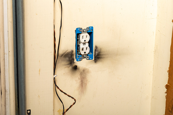 An electrical outlet has burn marks on the wall from a short circuit.