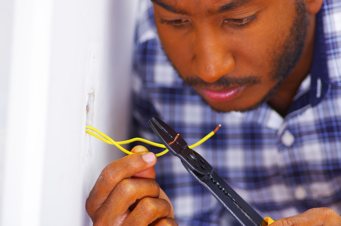 An electrician trims excess copper wire in a wall socket to ready it for a new outlet.