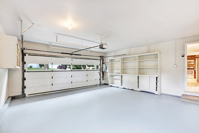 An empty garage with a white garage door and white storage shelves. 