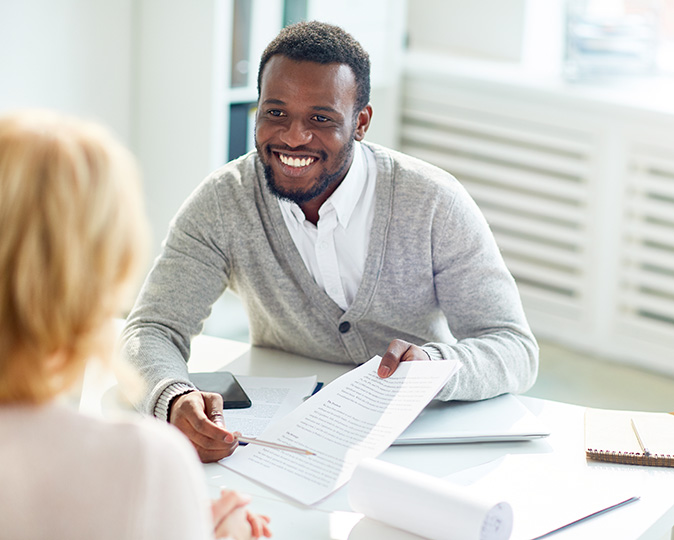A smiling man reviews paperwork with a woman at his desk.