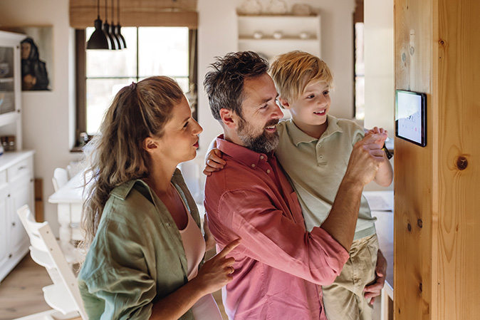 Modern programmable thermostat being adjusted by a father, mother, and child.