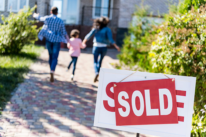 A family excitedly runs past the "Sold" sign into their new home.